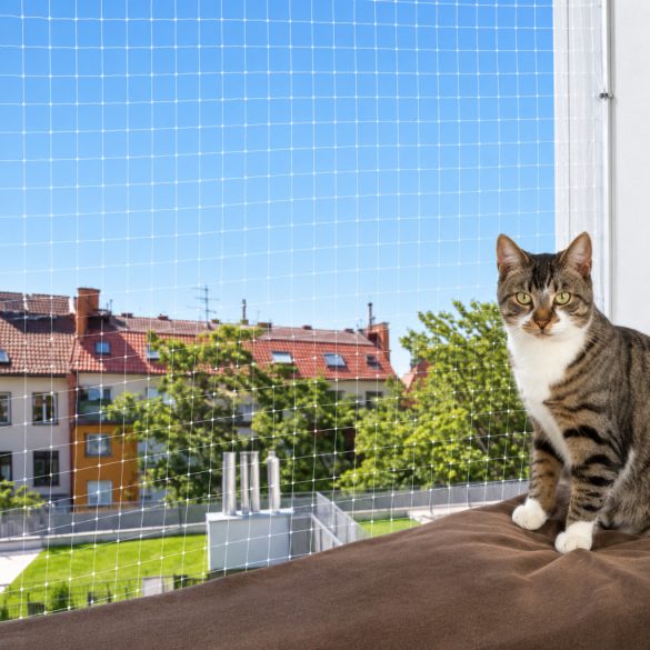 Fehér macskavédő háló erkélyen, mellette ülő cirmos macskával.